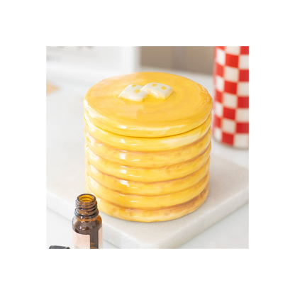 Pancake-stack ceramic oil burner with glossy yellow glaze and syrup finish on a marble surface, oil bottle