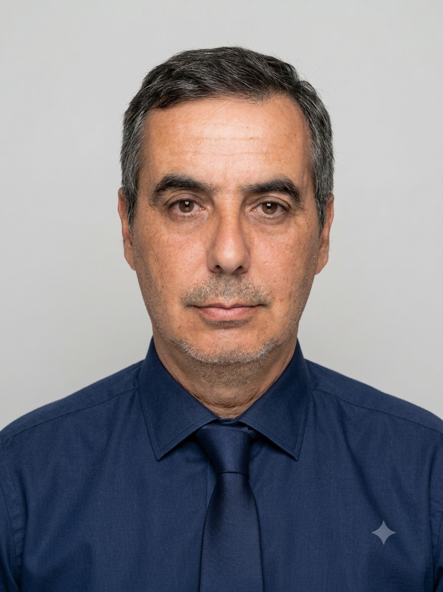 A man with short gray hair wearing a dark navy blue dress shirt and matching tie, photographed against a plain light gray background.