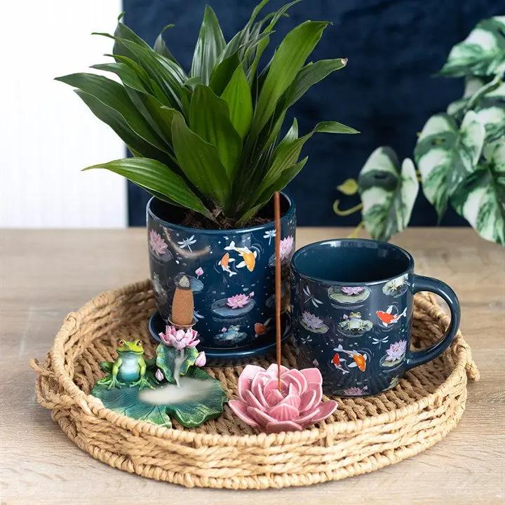 Decorative set with a potted plant, mug, and small figurines on a woven tray.