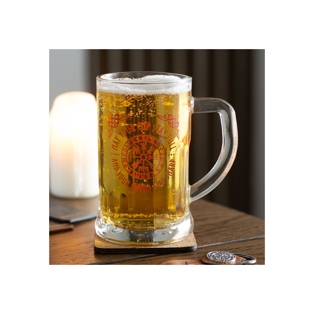 Glass mug with beer on a wooden surface with a candle in the background