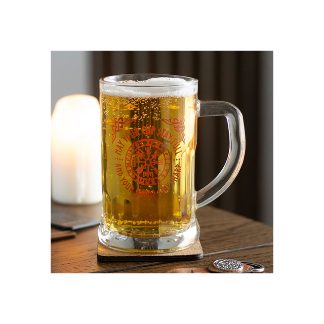 Glass mug with beer on a wooden surface with a candle in the background